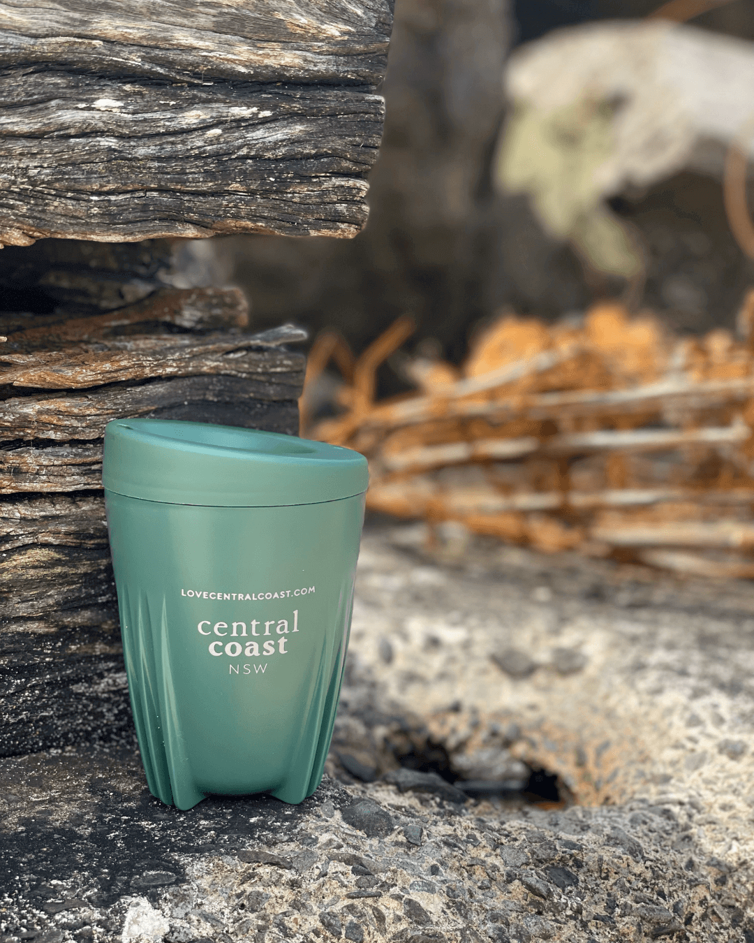 reusable coffe cup at the beach rocks