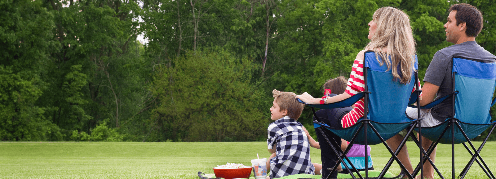 A family of four enjoying an outdoor movie on a green field
