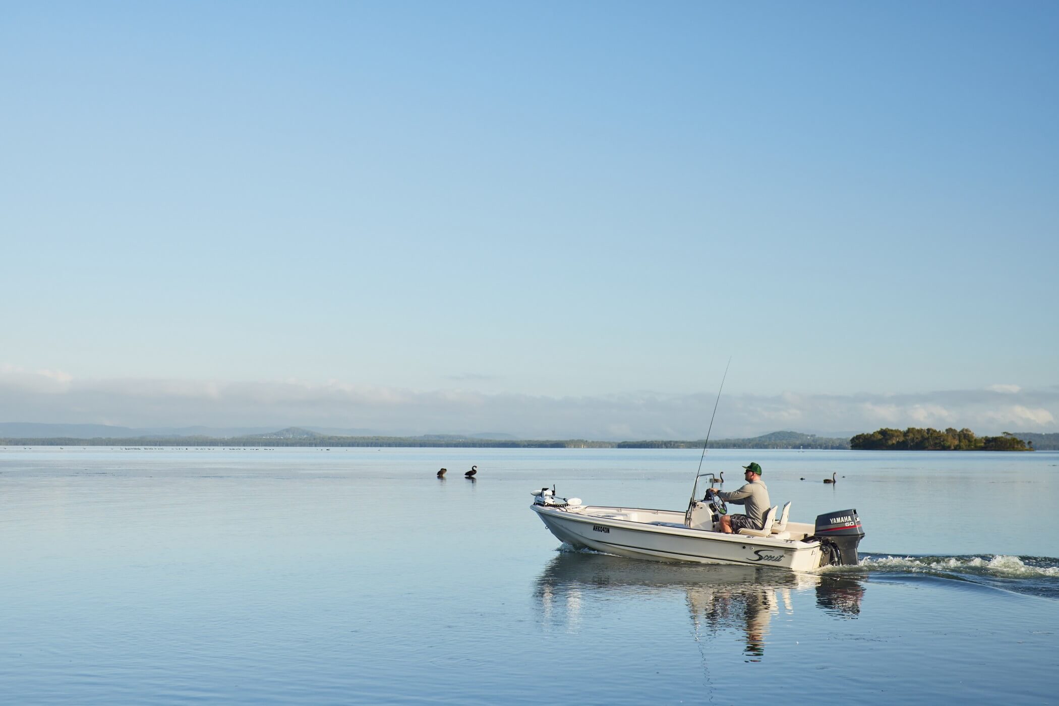 person fishing on calm lake in small tinny