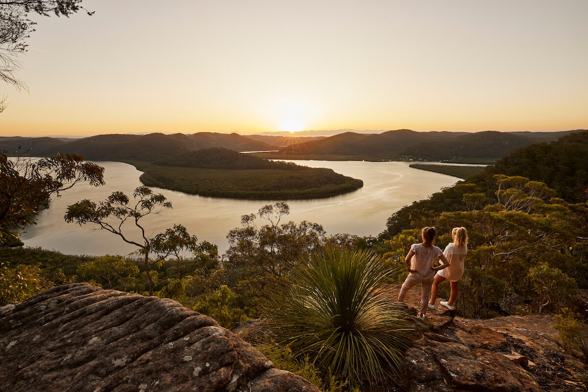 two people on rocky lookout at sunset peering over waterways