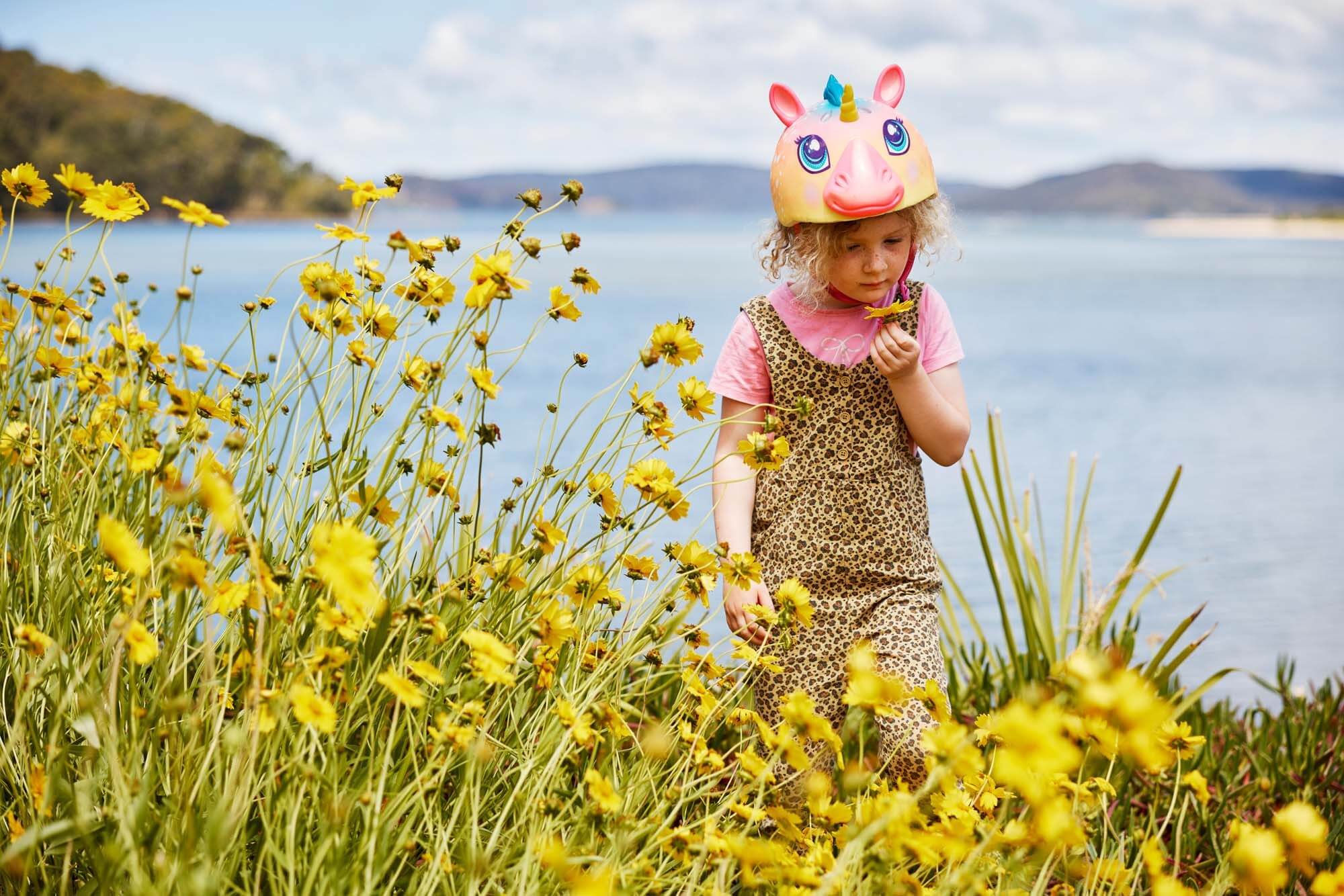 young child smelling the wildflowers on edge of water