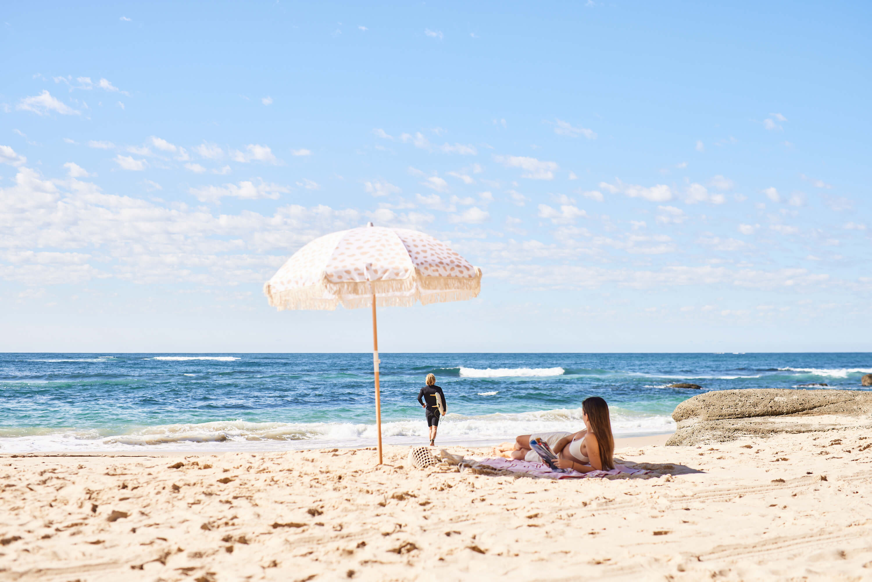 couple sunbathing under umbrella and running to surf