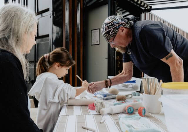 A man wearing a bandana teaches a little girl how to sculpt clay