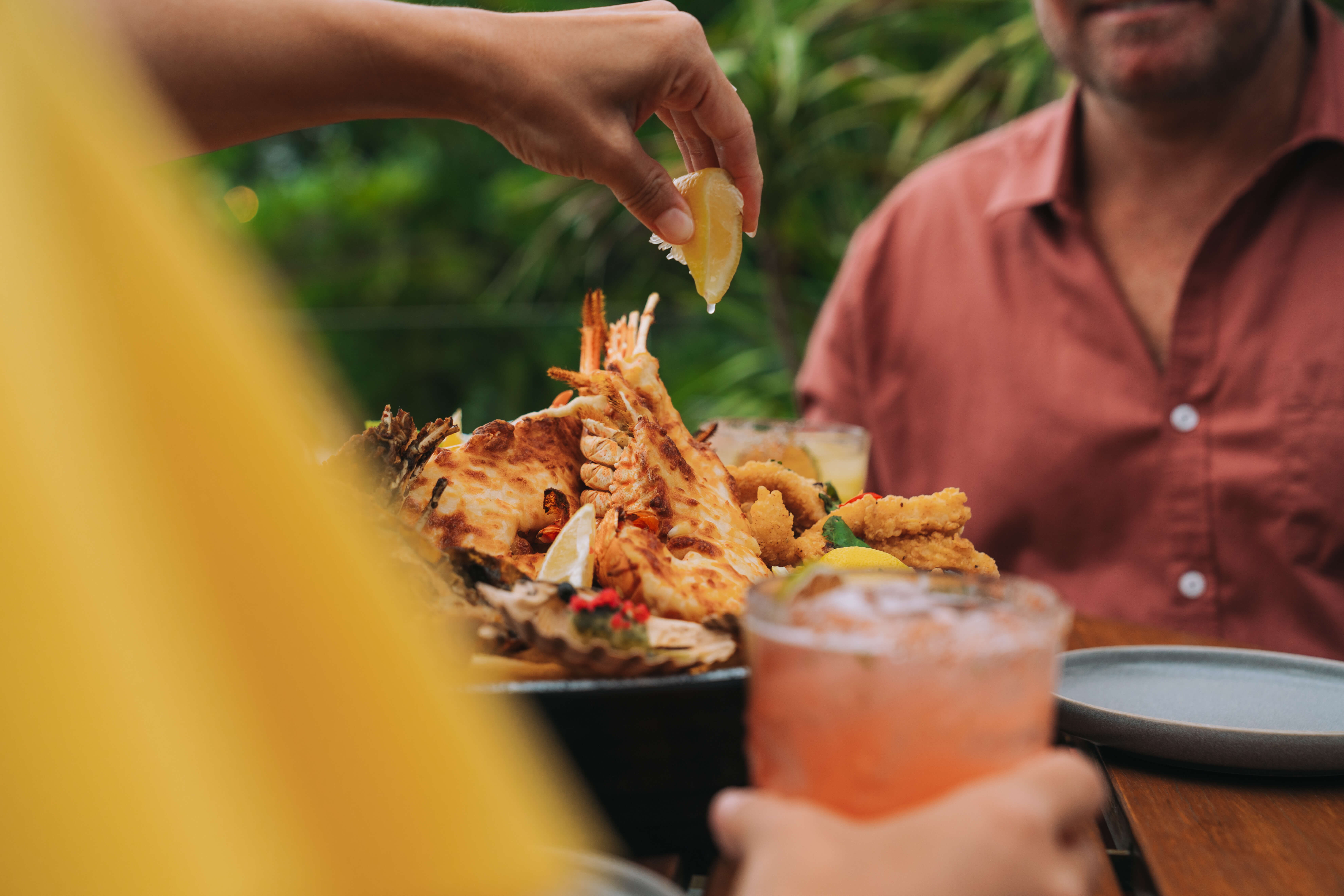 A lady squeezing a wedge of lemon ofer a plate of cooked seafood