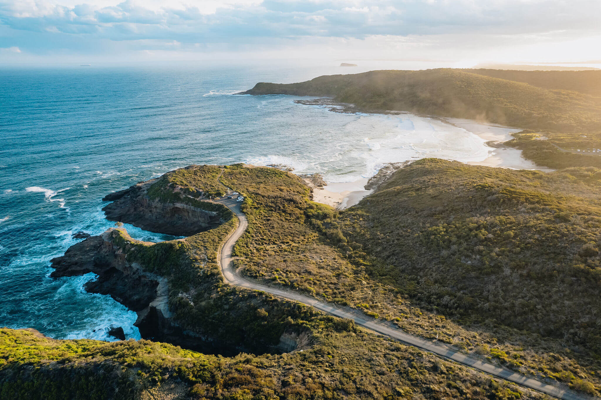 Photo of road to a headland surrounded by lush green bushland overlooking the blue-green open ocean