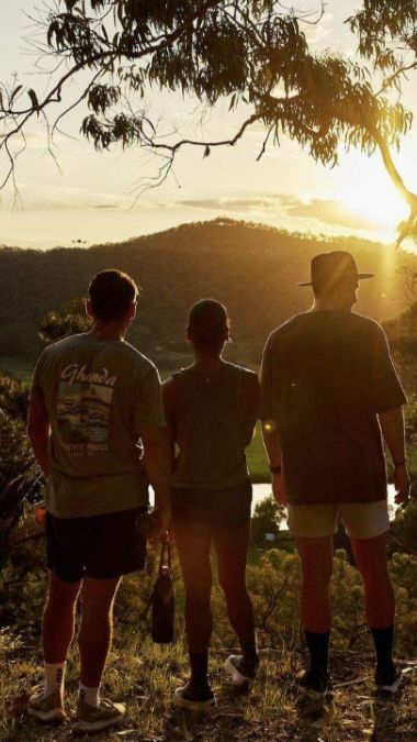 three friends watching the sunset over the mountains