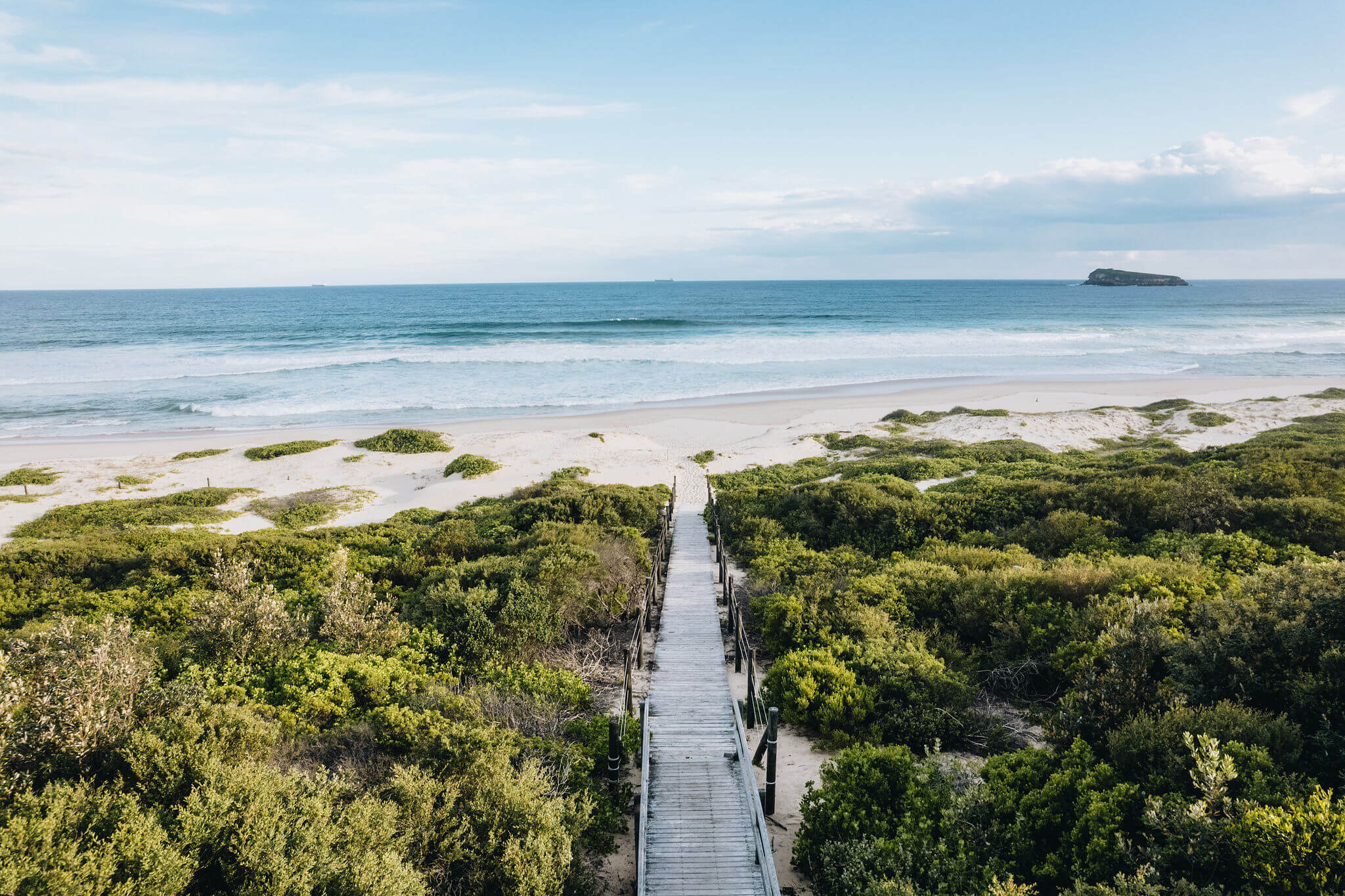 aerial of pristine beach with wooden path leading onto sand