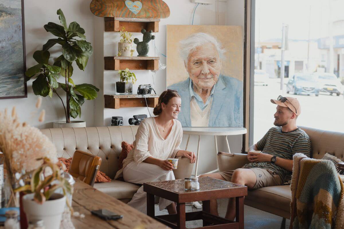 couple enjoying cafe vibes with portrait of sir david attenborough in background 