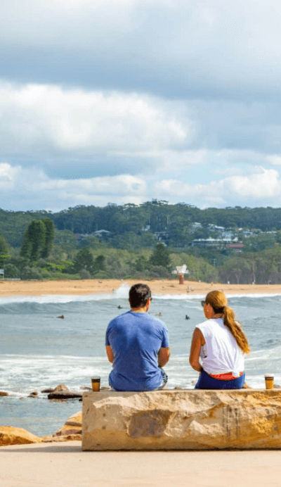 Couple sitting on wall over looking Avoca Beach NSW