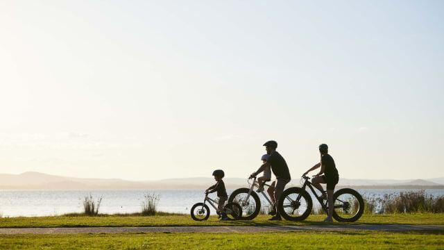 family of three cycling beside lake on shared path
