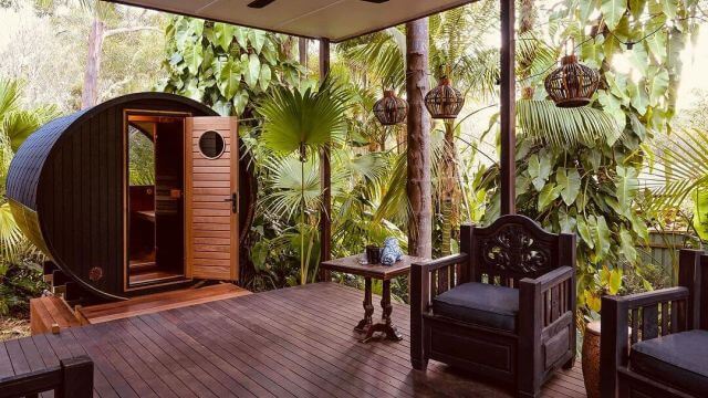 Round, wooden sauna on a deck surrounded by lush tropical foliage