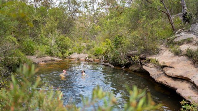 two people wild swimming in emerald pool