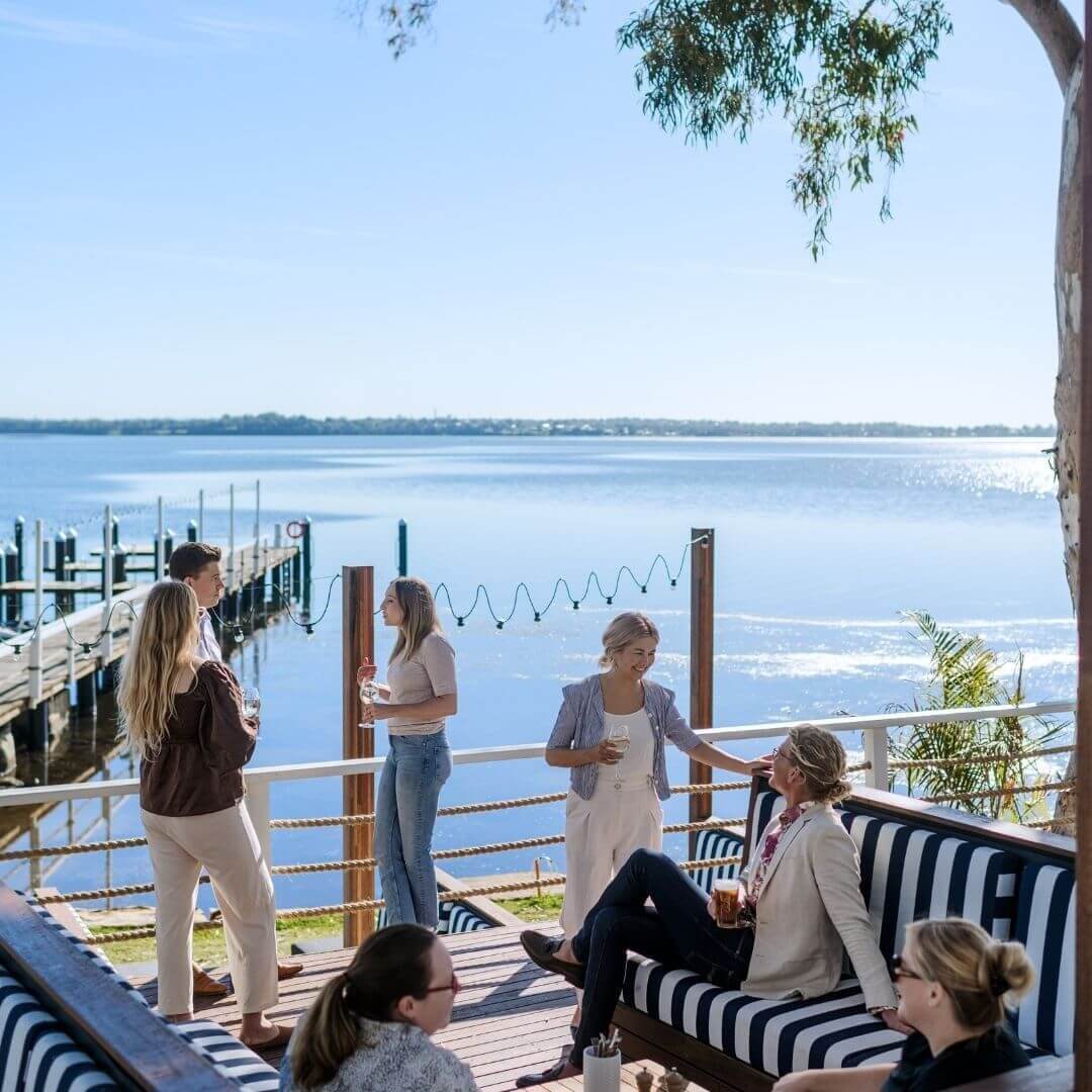 millenials socialising on lakeside deck with drinks 