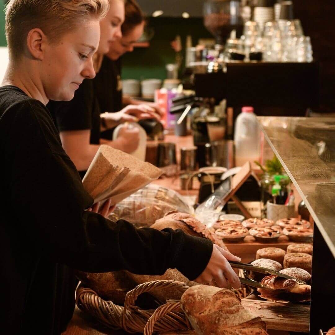 staff serving pastries behind scenes of busy cafe