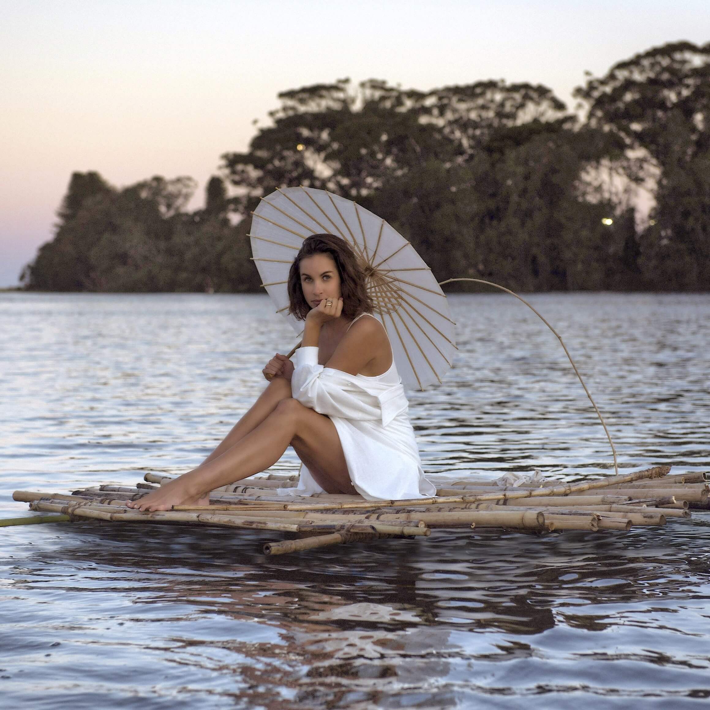 female artist afloat on handbuilt raft with stylish umbrella