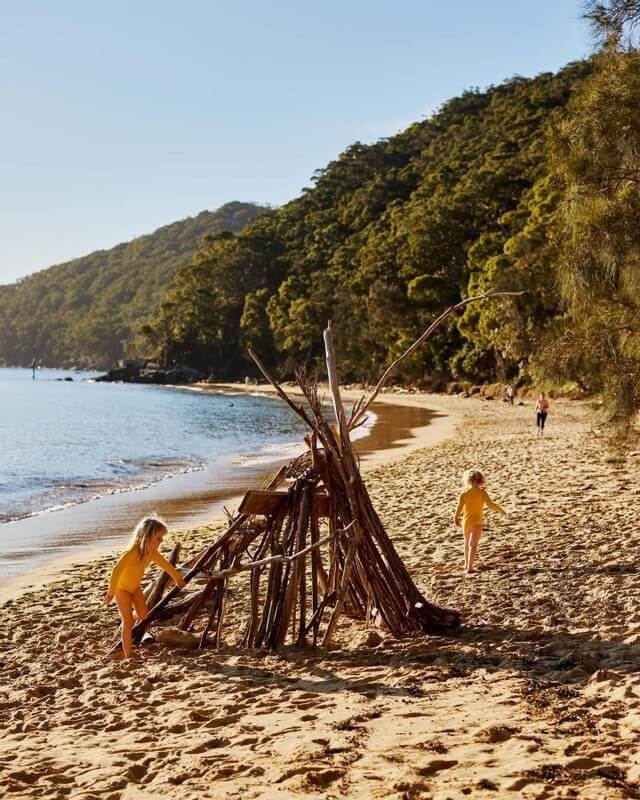 two kids play around stick hut on beach