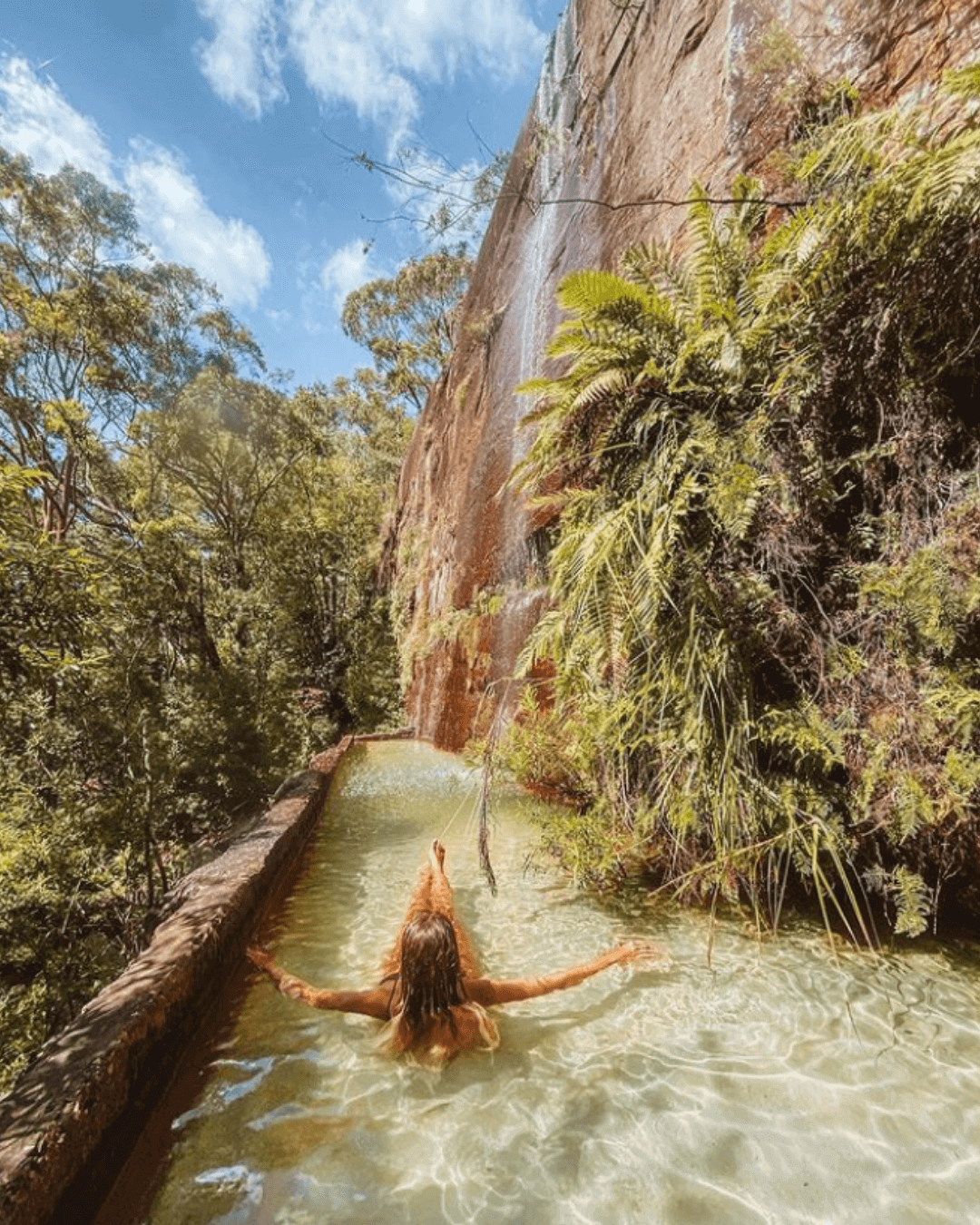 woman bathing in tropical trough below waterfall