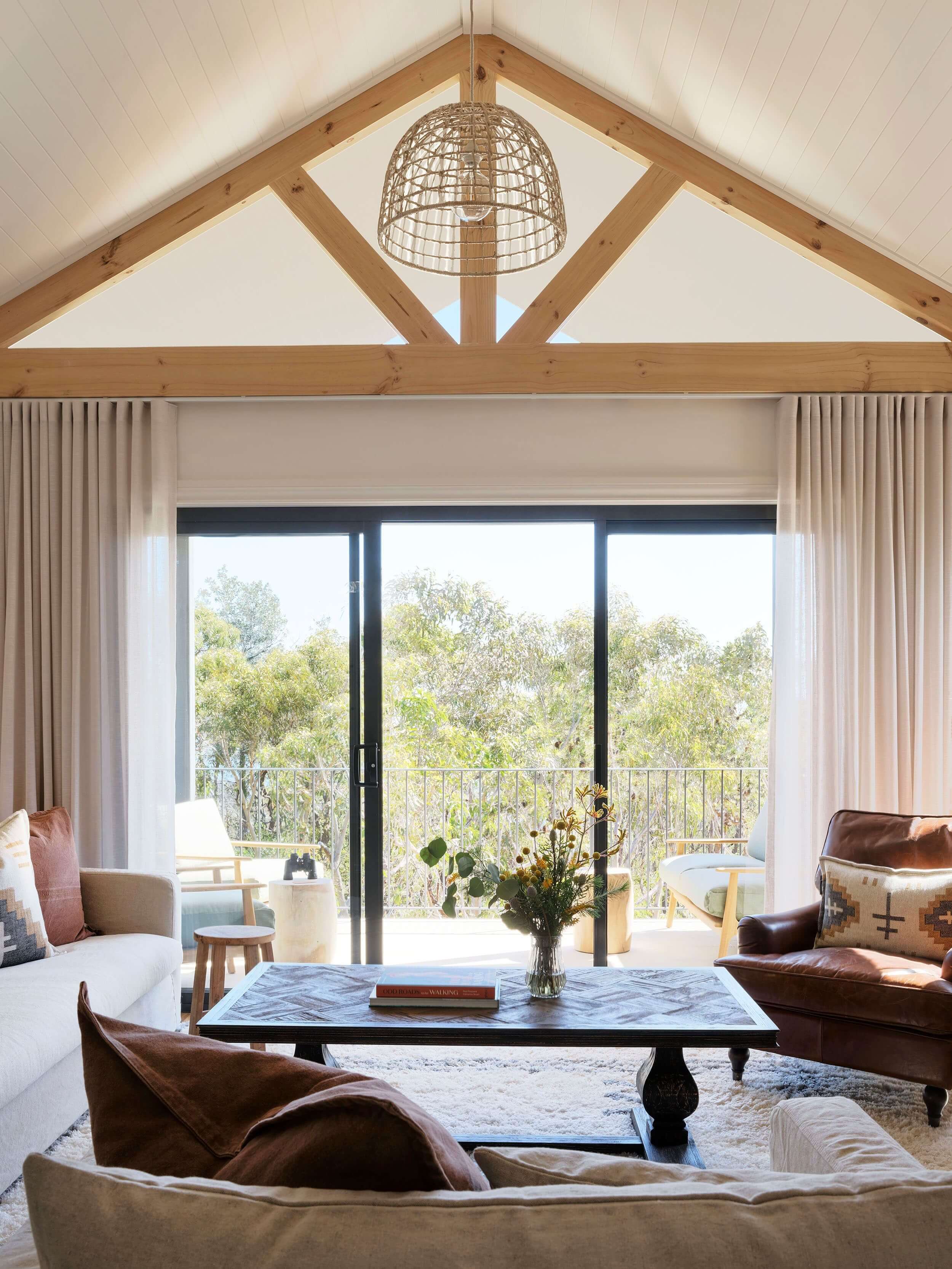 Cream, white and wood themed living area in a lodge looking out to the deck to the bush