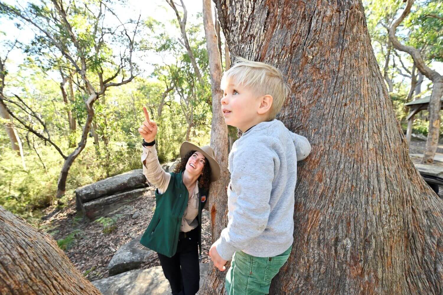 Ranger in bushland point and telling a young blond boy about the plants in the bushland