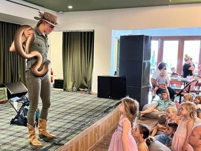 Snake handler on stage with a python around her arms talking to a group of kids in a function room at Budgewoi Hotel.