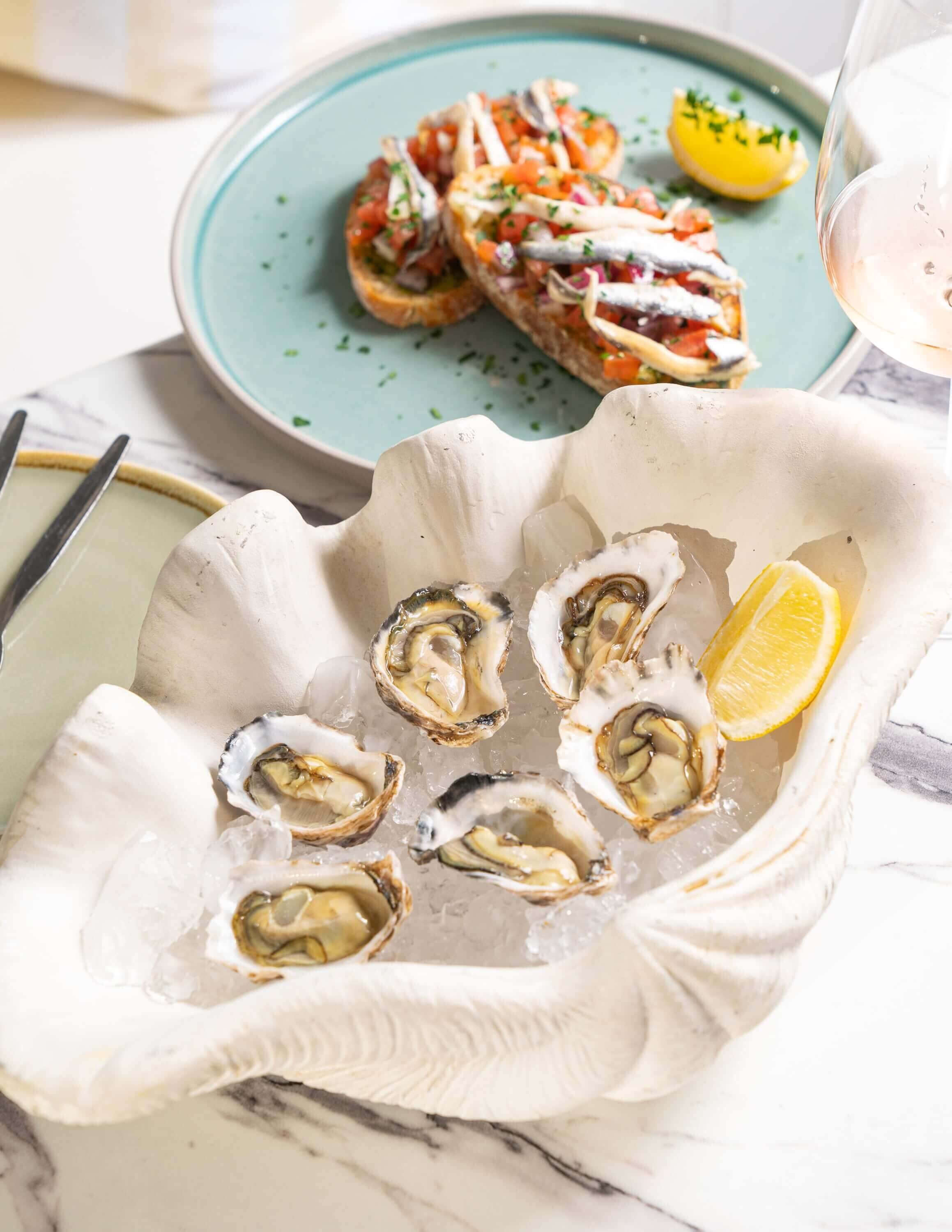 Six oysters in a large white shell and two slices of bruschetta on a light teal plate.