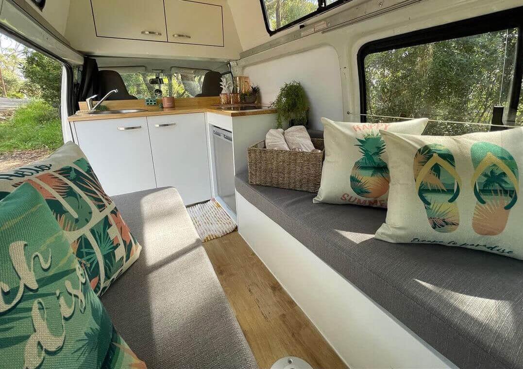 Inside of a luxury van with green themed cushions with the view of bushland in the background