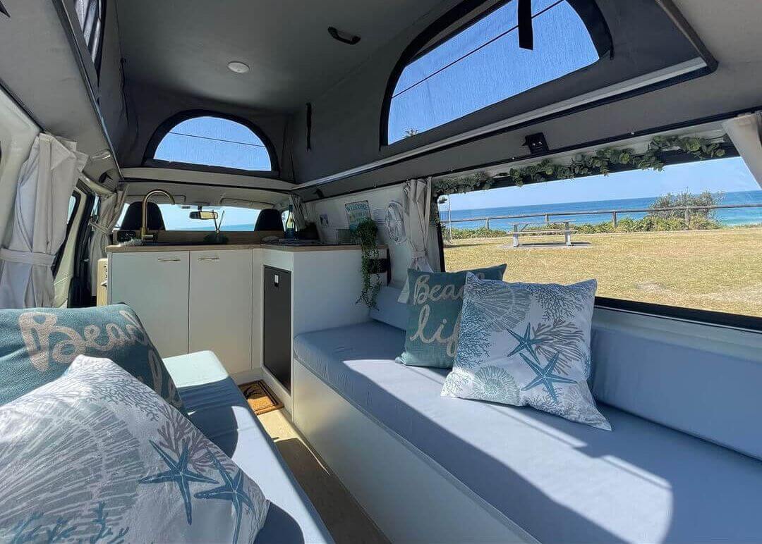Inside of a blue and white theme luxury van with the view of the sand and ocean in the background