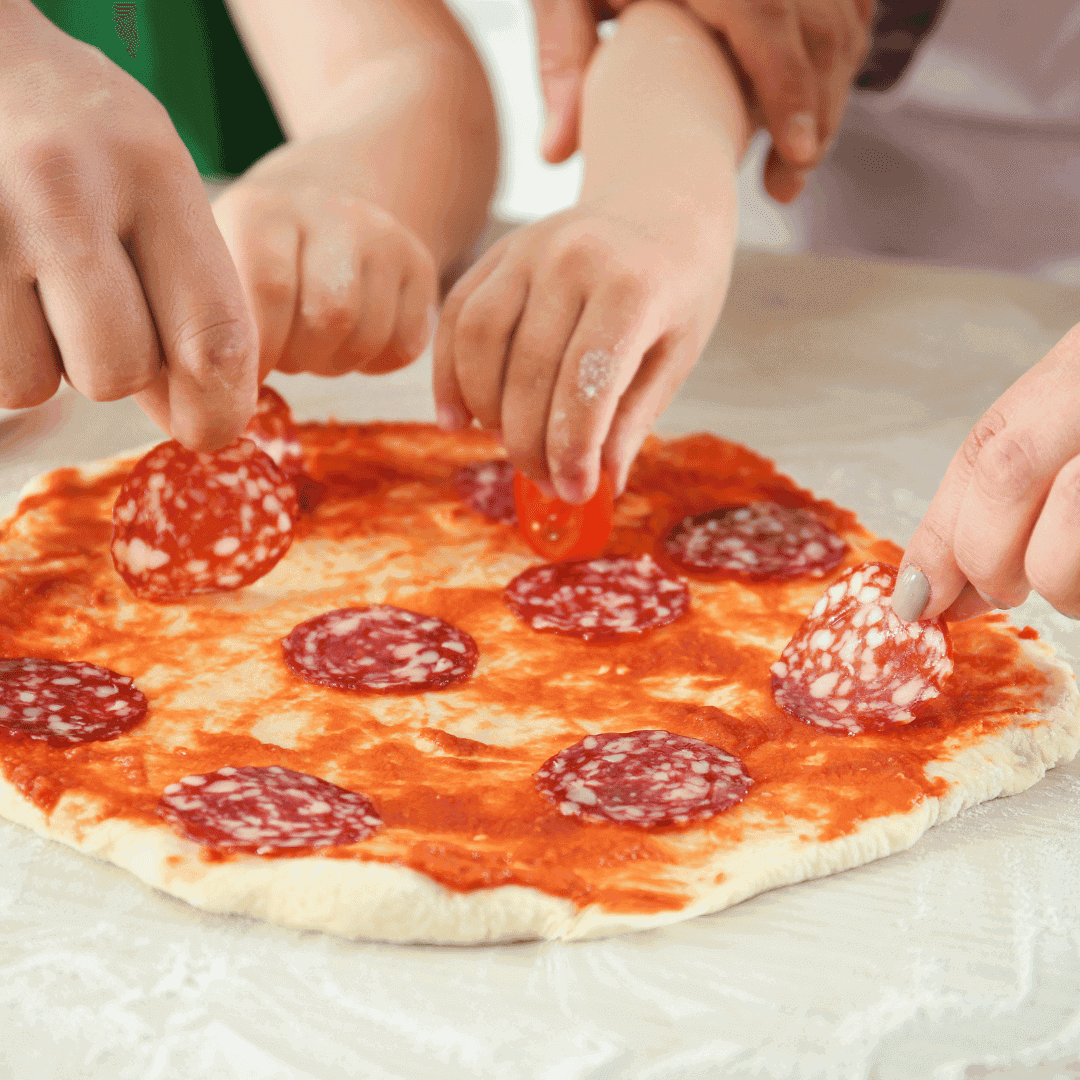 Kids hands making a pepperoni pizza.