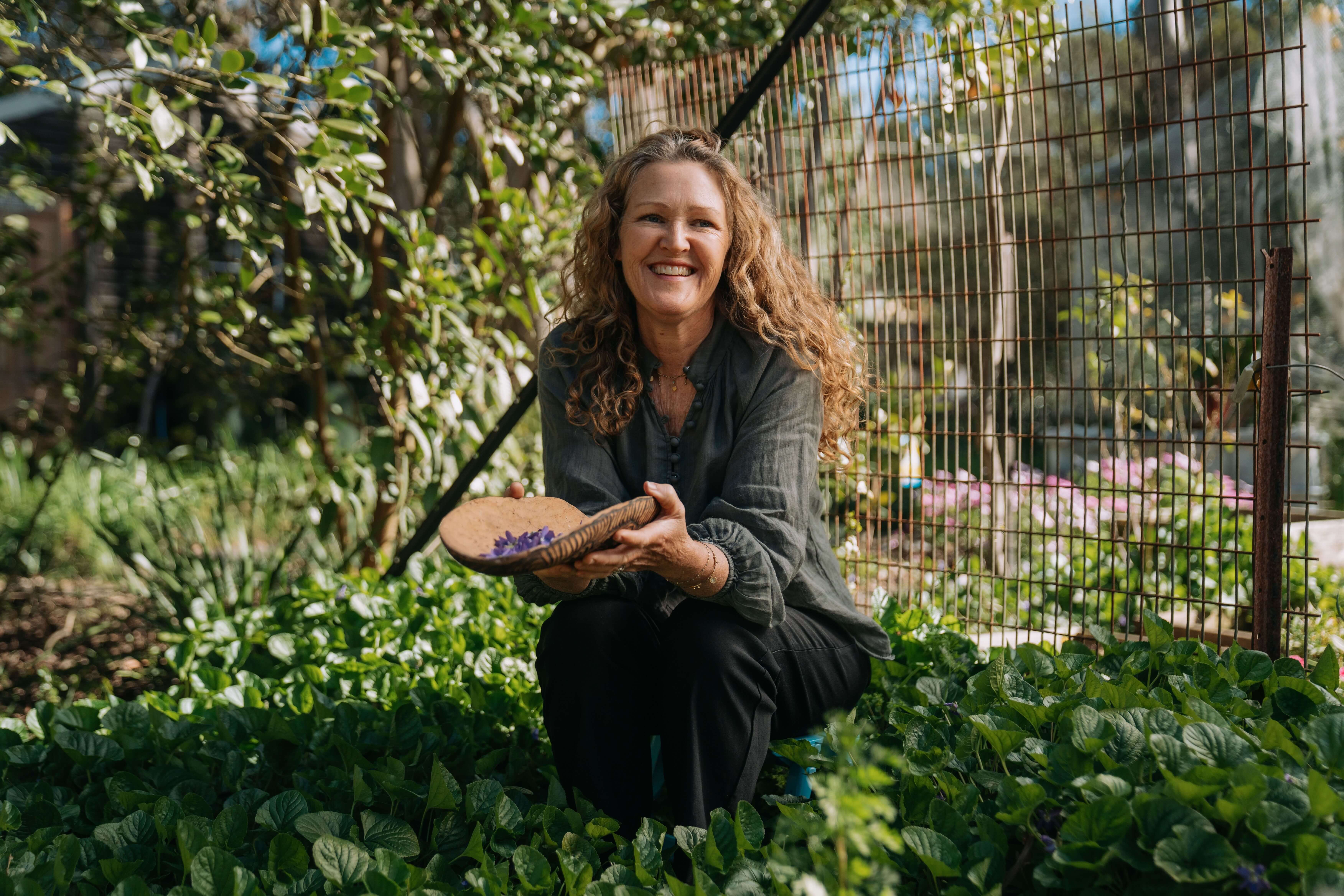 winemaker crouching in her permaculture led organic garden with a bowl of foraged botanicals