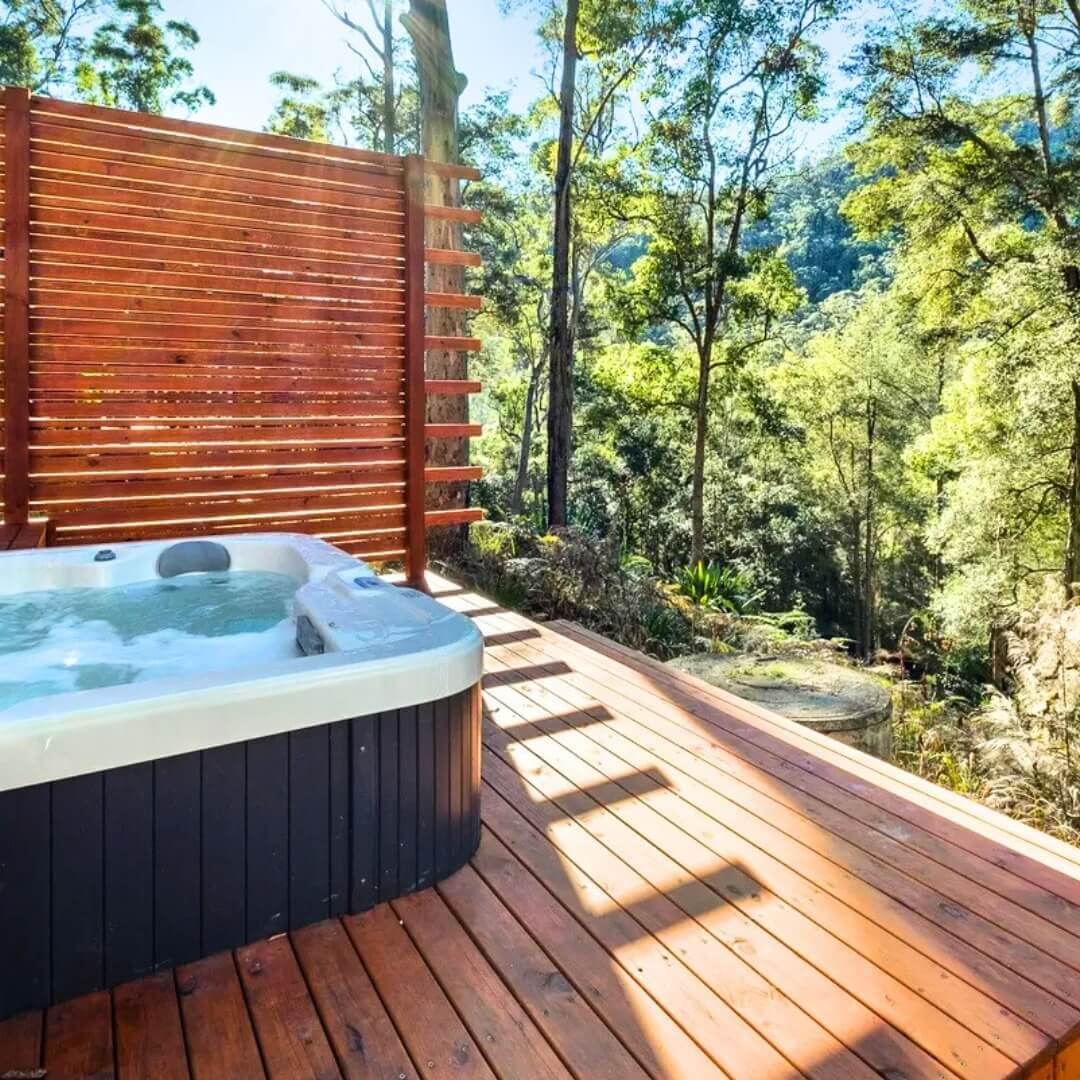 A bubbling outdoor spa sitting on a wooden deck, overlooking the bush