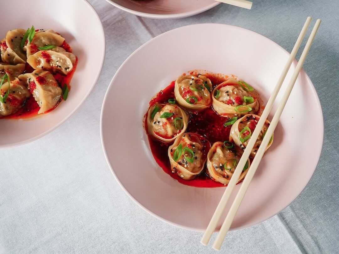 A bowl of 6 dumplings surrounded by a chilli broth and chopsticks lay across the top of the bowl