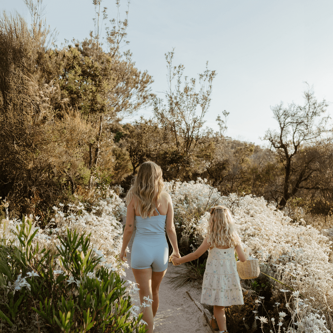 A mum and daughter walking through bushland with native white wildflowers blooming either side of the trail