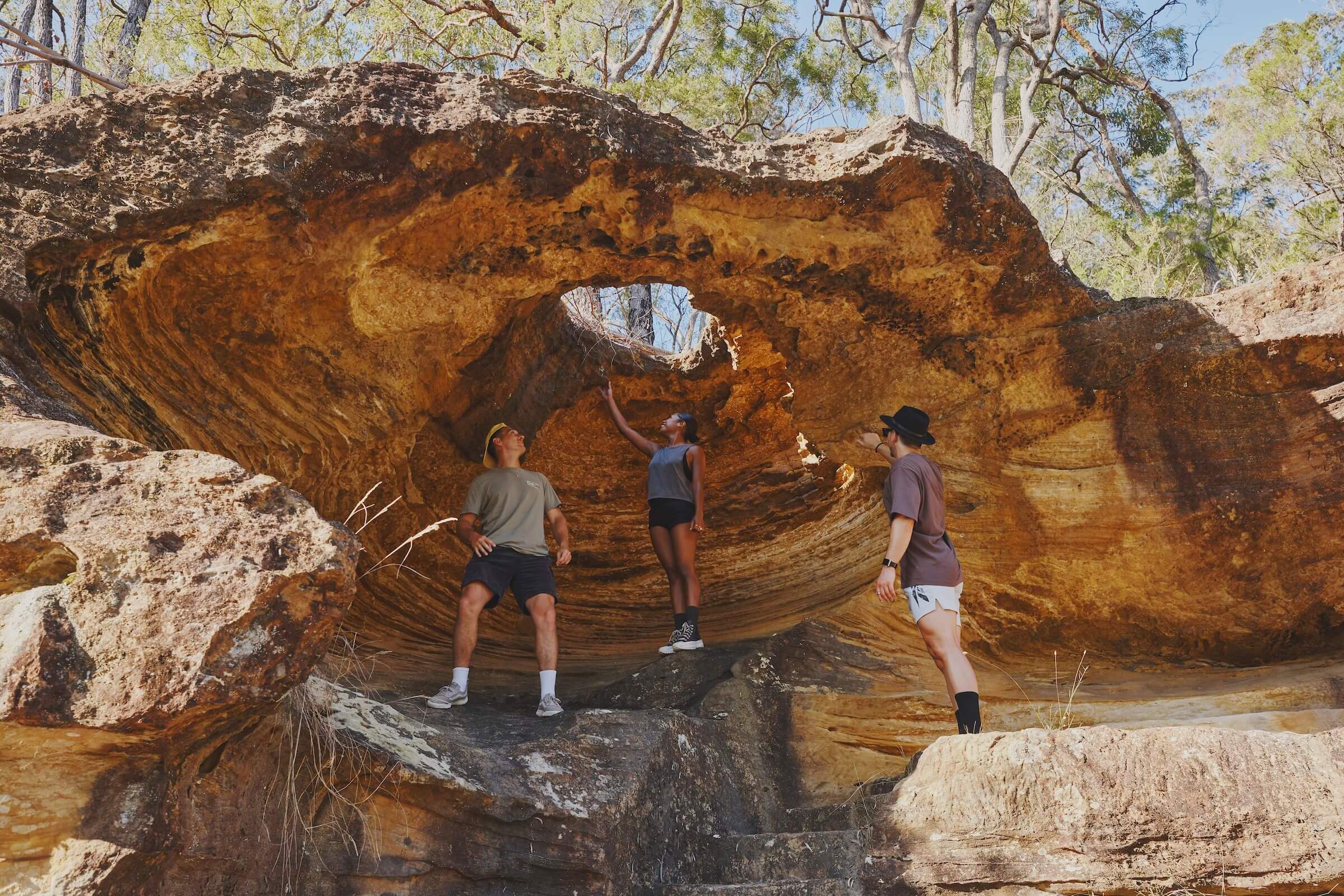Three people standing under a sandstone rock overhang formation with a hole in the top.