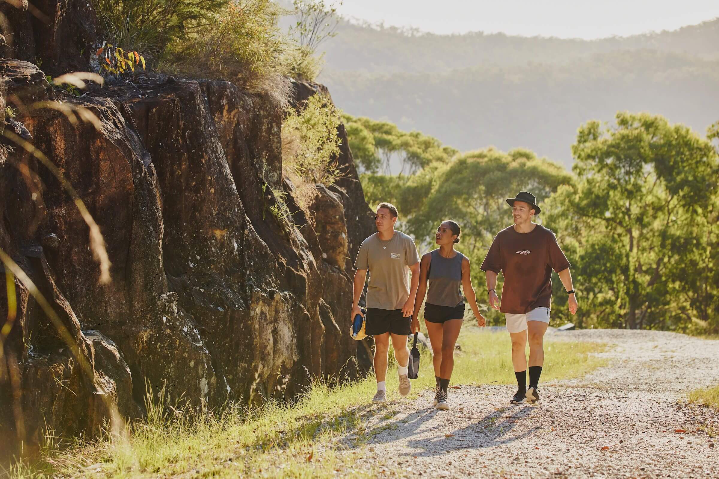 Three people walking up a gravel road with a rock wall to the left of them