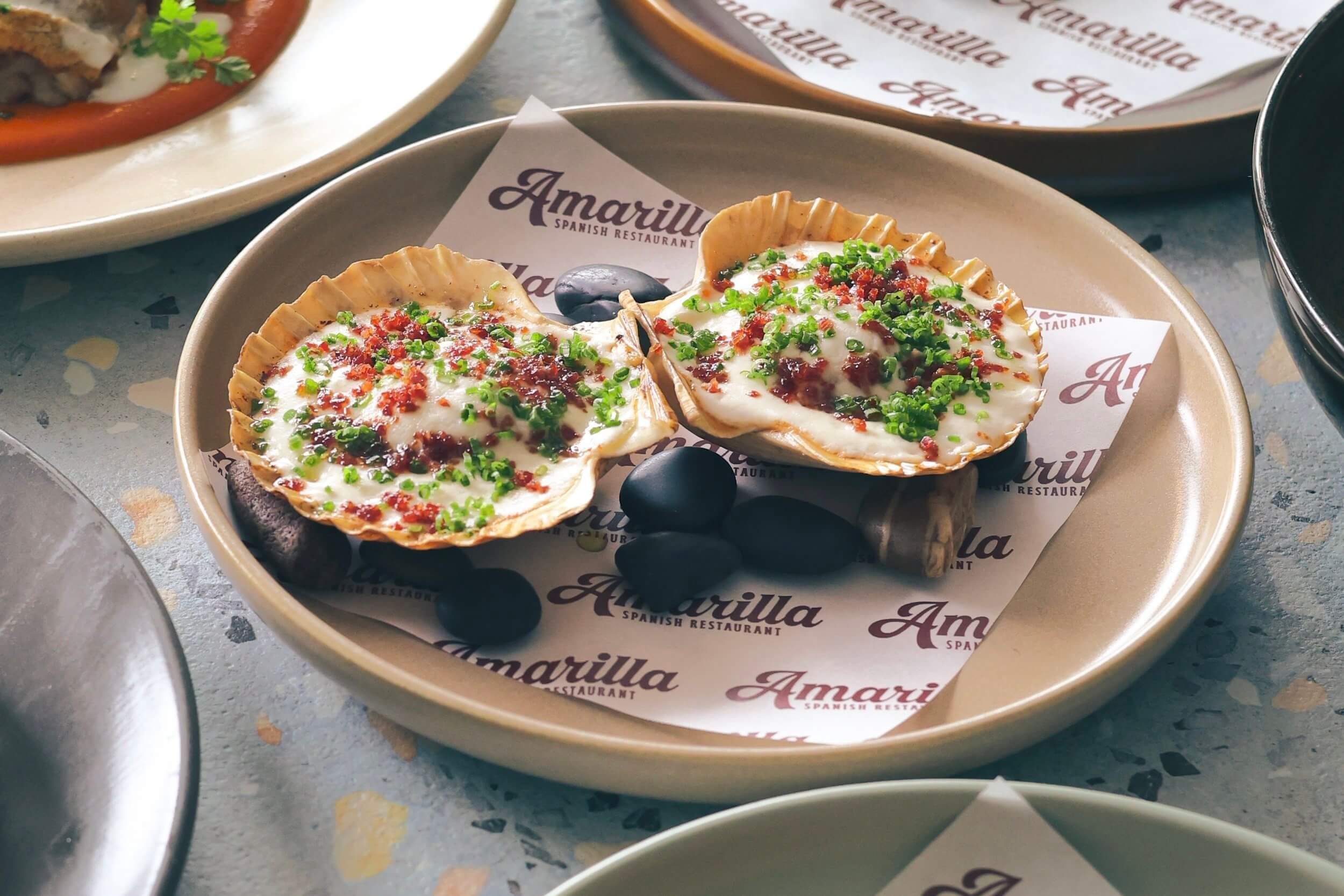 A plate with two scallops topped with cauliflower puree and chives