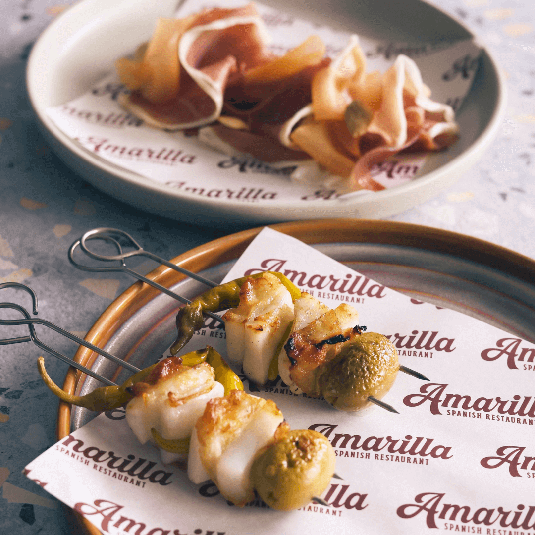Two metal skewers with calamari, green olives and green chillis