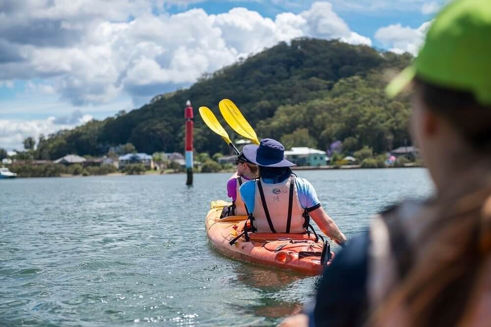 Two individuals paddling in a colourful kayak on a calm body of water under a clear blue sky