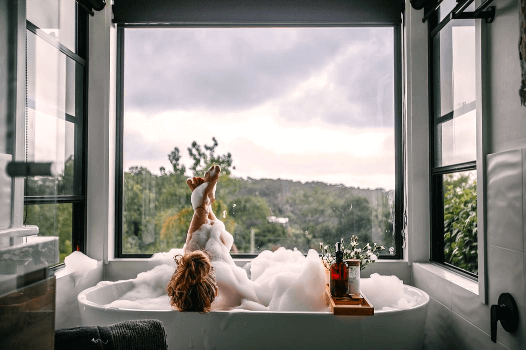 A woman enjoys a relaxing bath, surrounded by bubbles, creating a serene and tranquil atmosphere with a valley view.