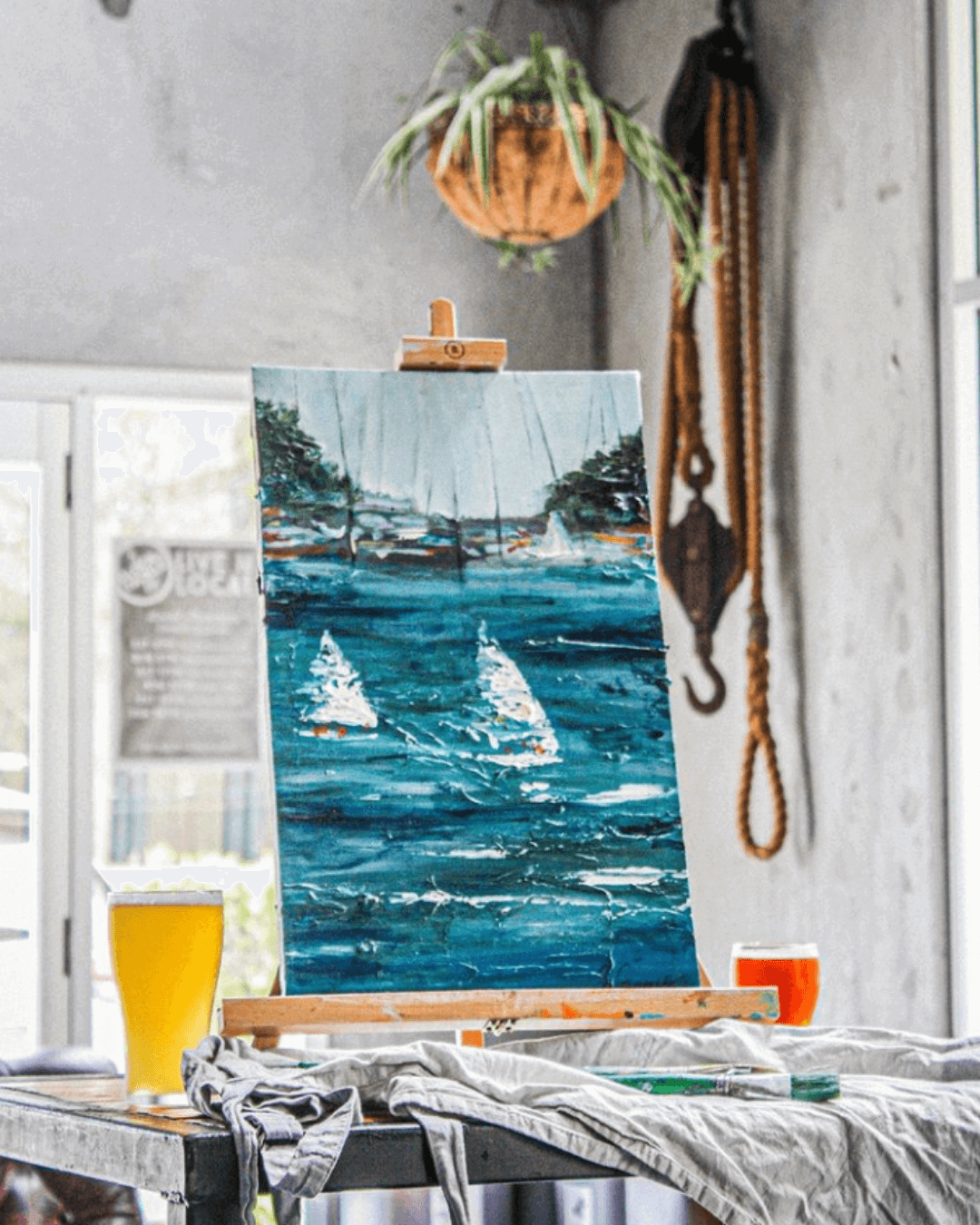 painting of boats on water with a craft beer beside