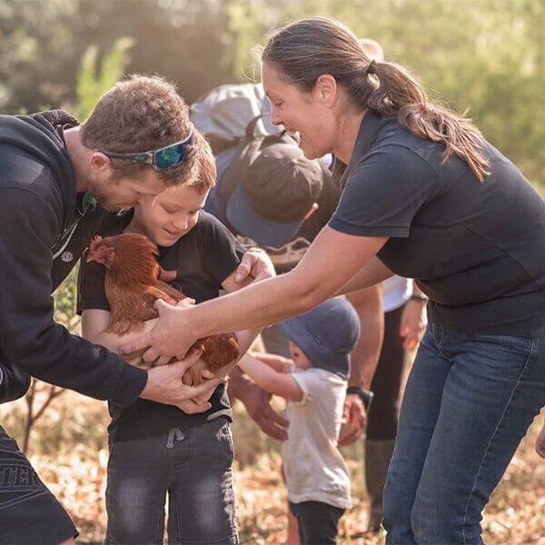 woman shows kids chicken handling on farm