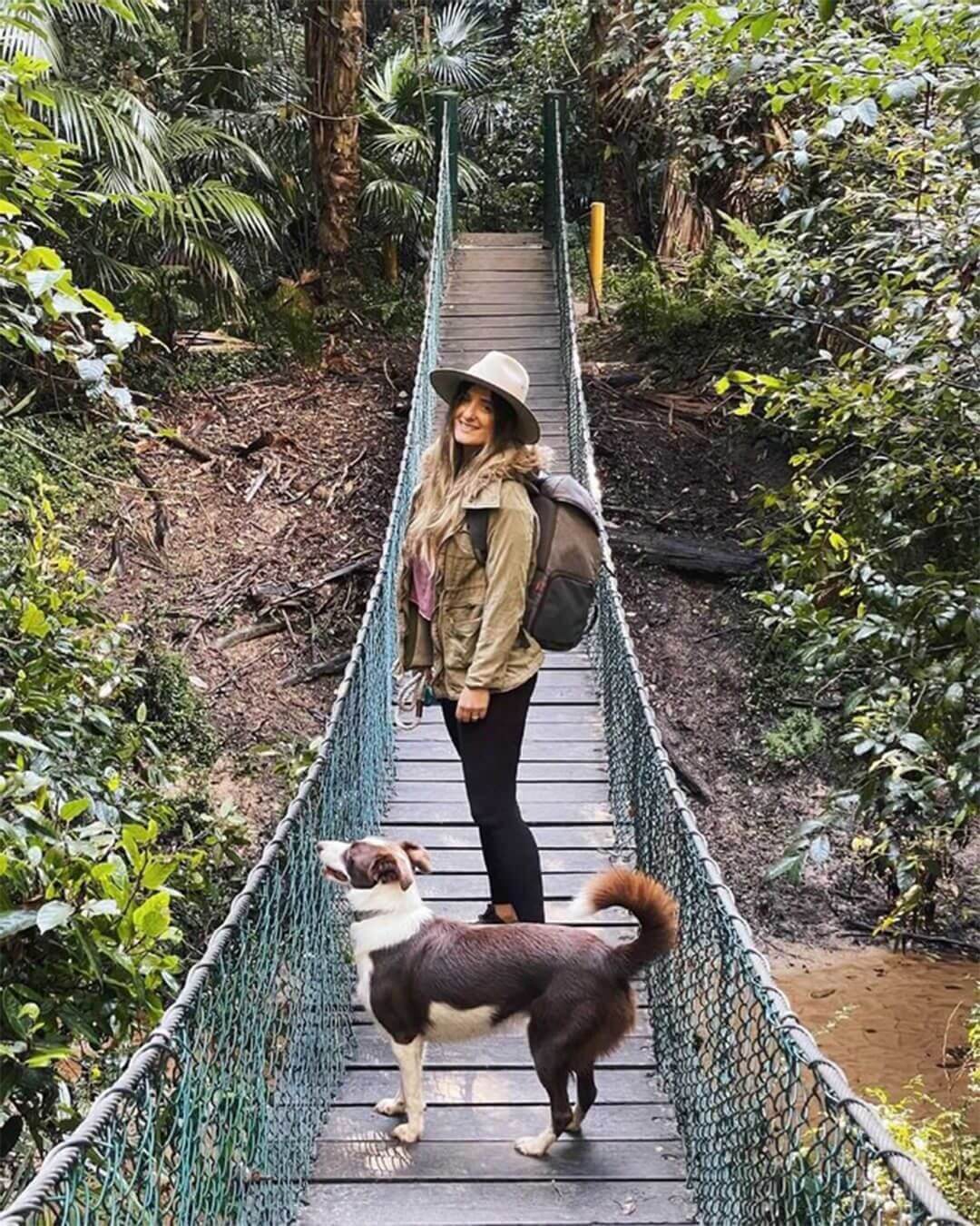 woman and dog hiking across forest bridge