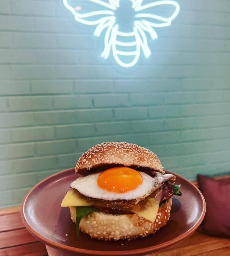 An image of an egg and bacon roll in front of a luminous Bees Knees logo on the wall inside the cafe