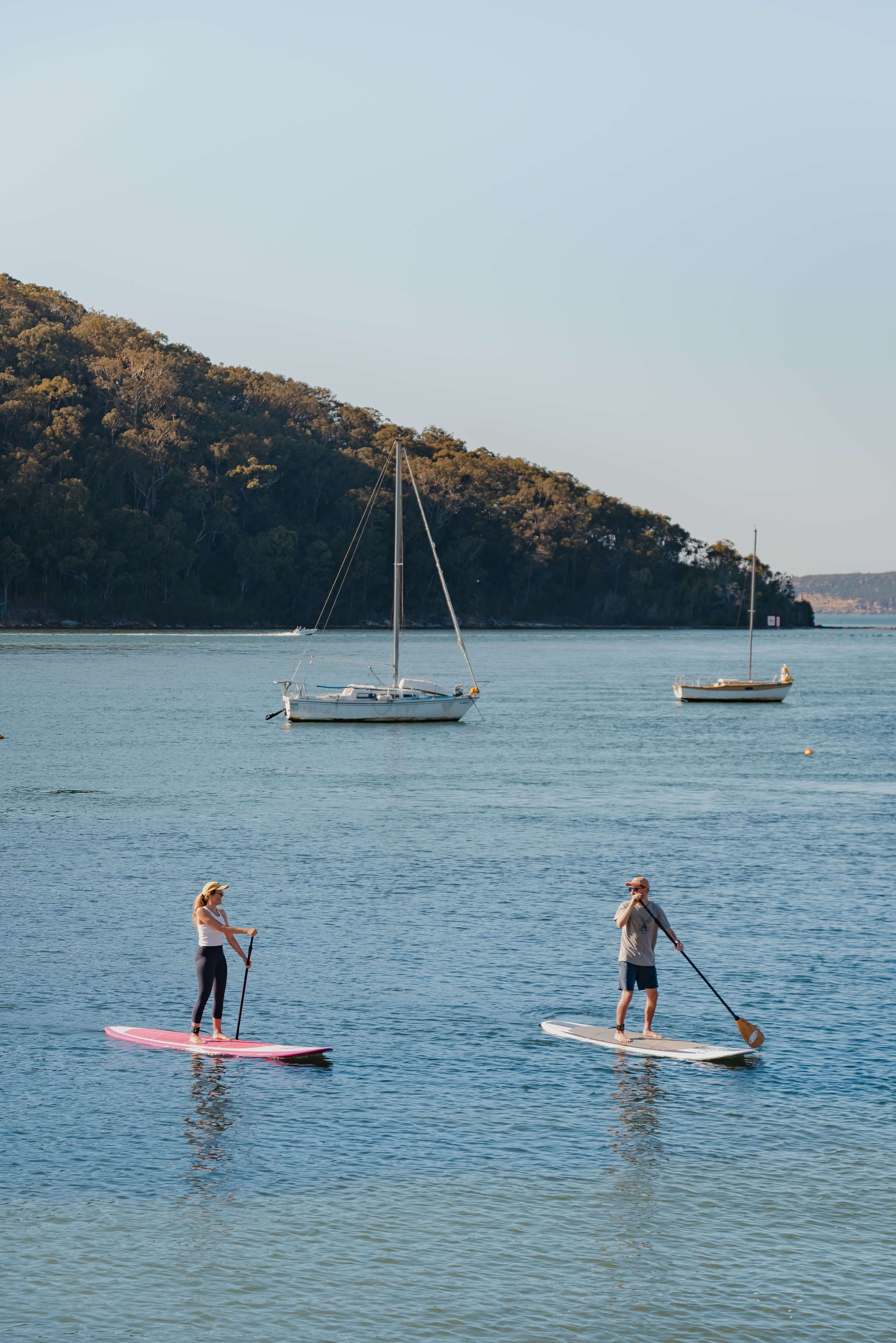 couple stand up paddle boarding on bay