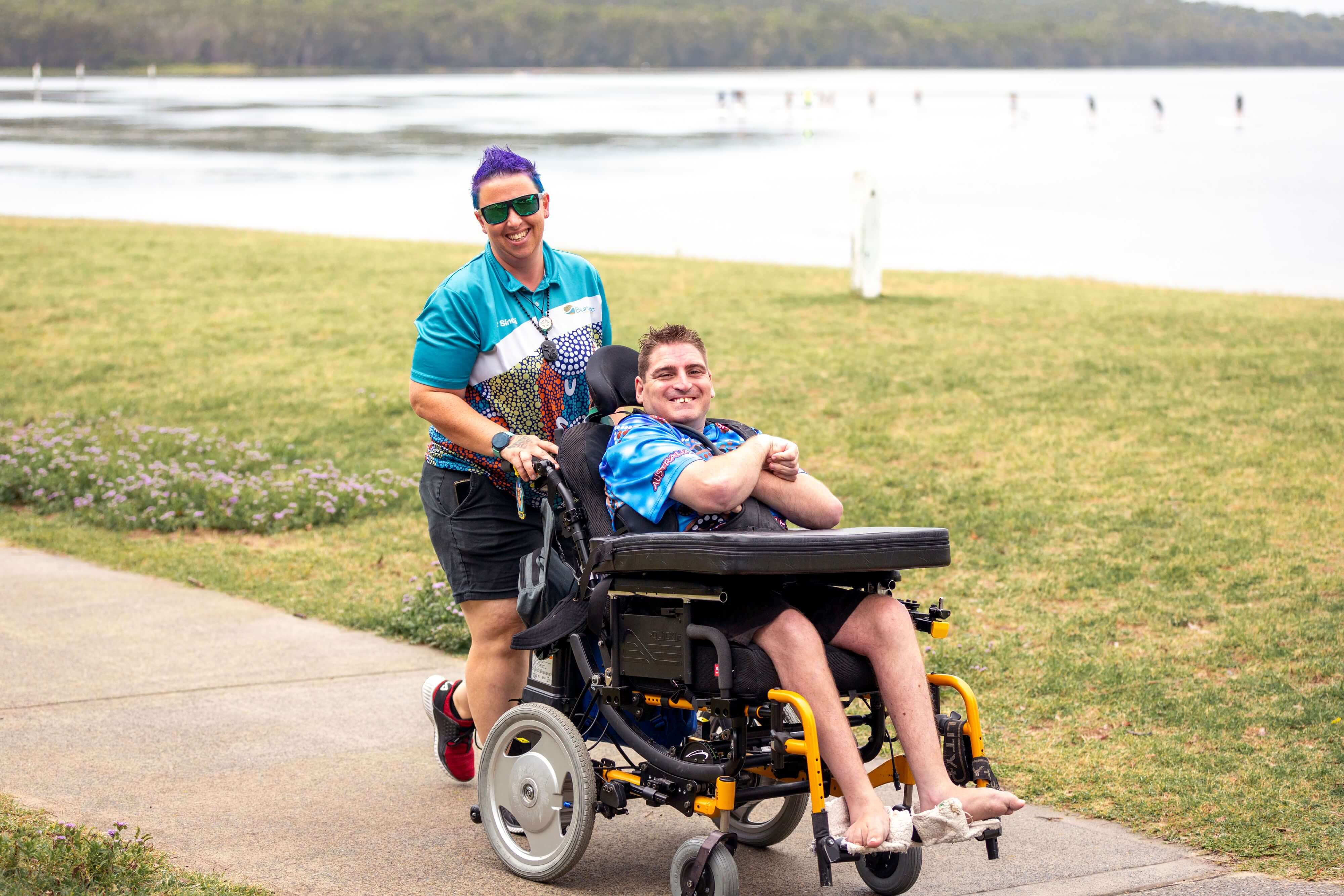 A support worker and person in a wheelchair travelling along Tuggerah Lake Foreshore shared pathway 