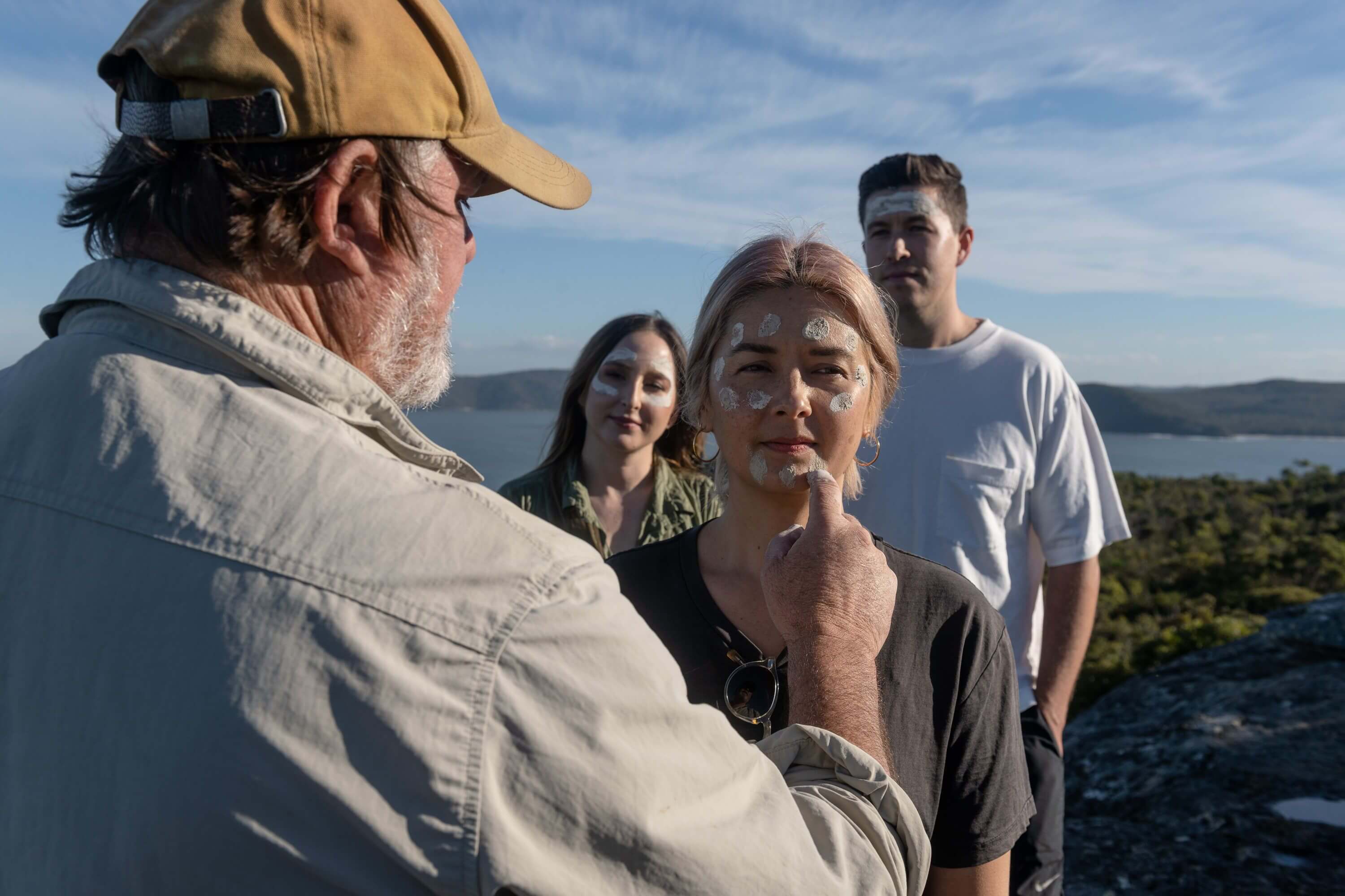 woman getting clay face paint by aboriginal man