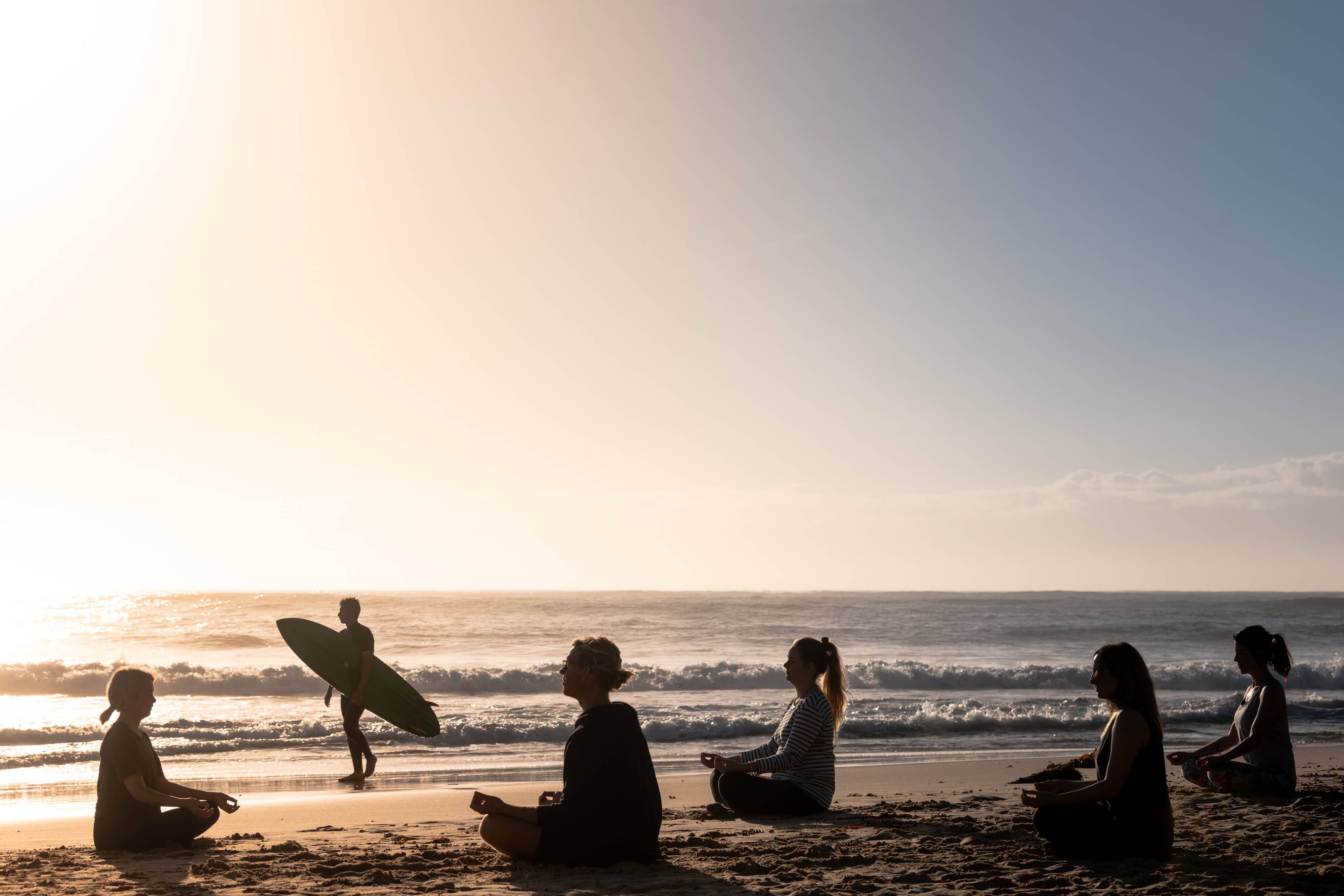 poeple doing yoga and surfing beachside at sunrise