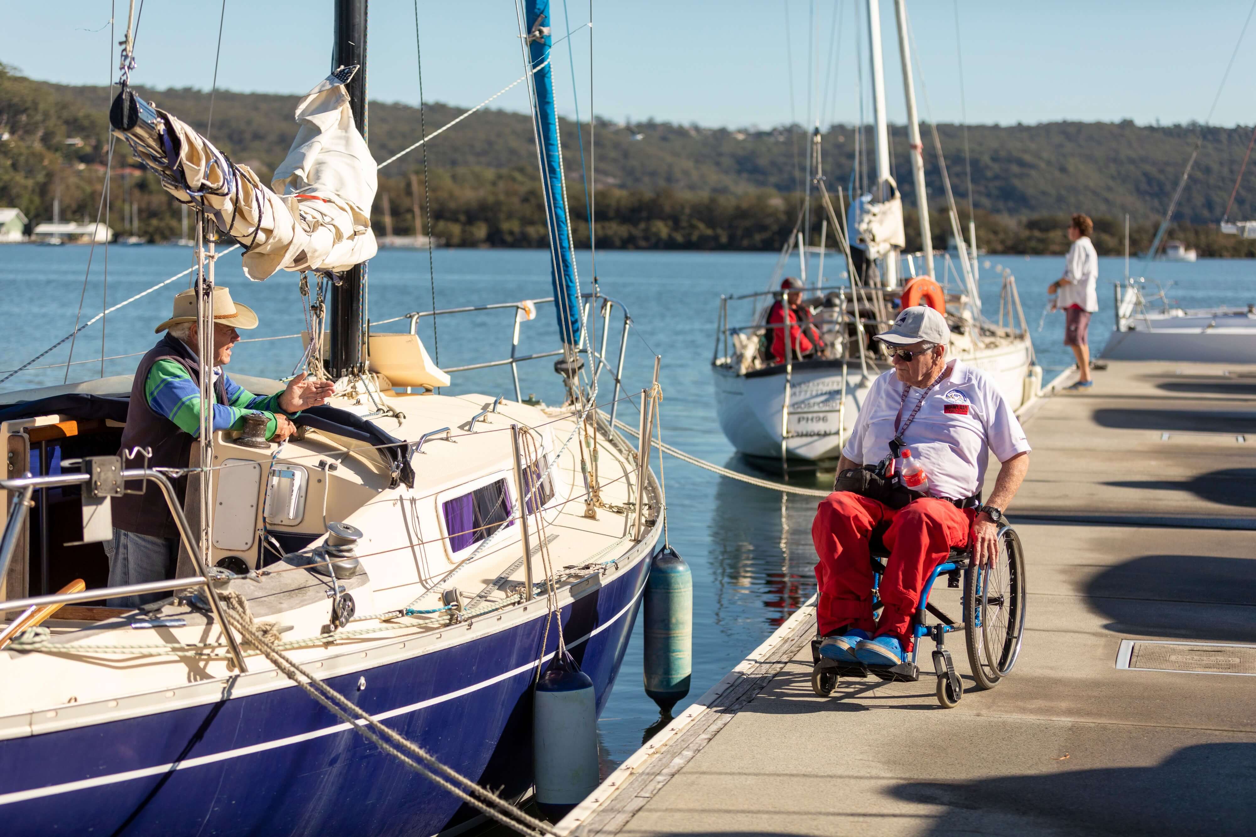Person in wheelchair on the marina talking to person on Yacht at Gosford Sailing Club 