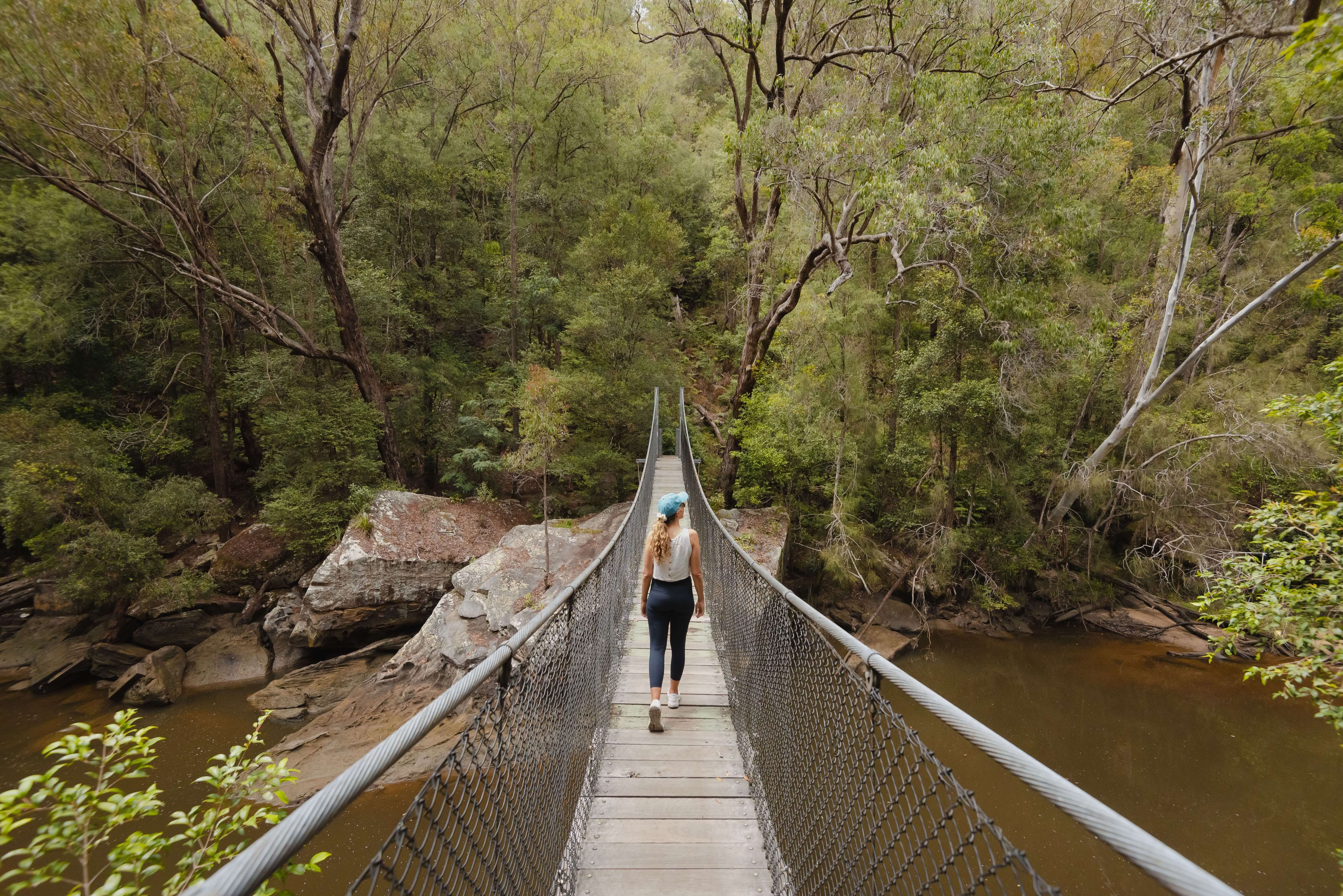 woman hiking across suspension bridge in bushland