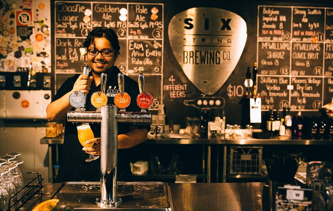 bloke serving beer from tap with chalkboard menu of beers behind