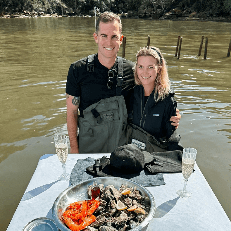 Couple in water infront of table with oysters Sydney Oyster Tours